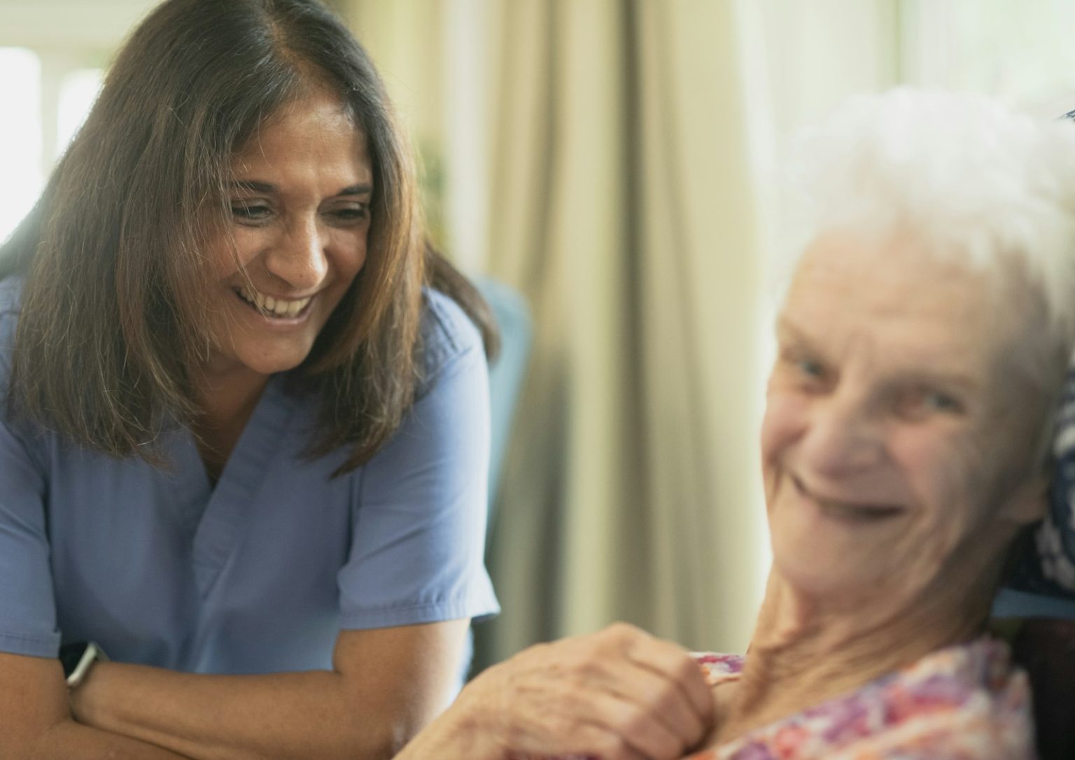 A smiling caregiver sitting with an older woman