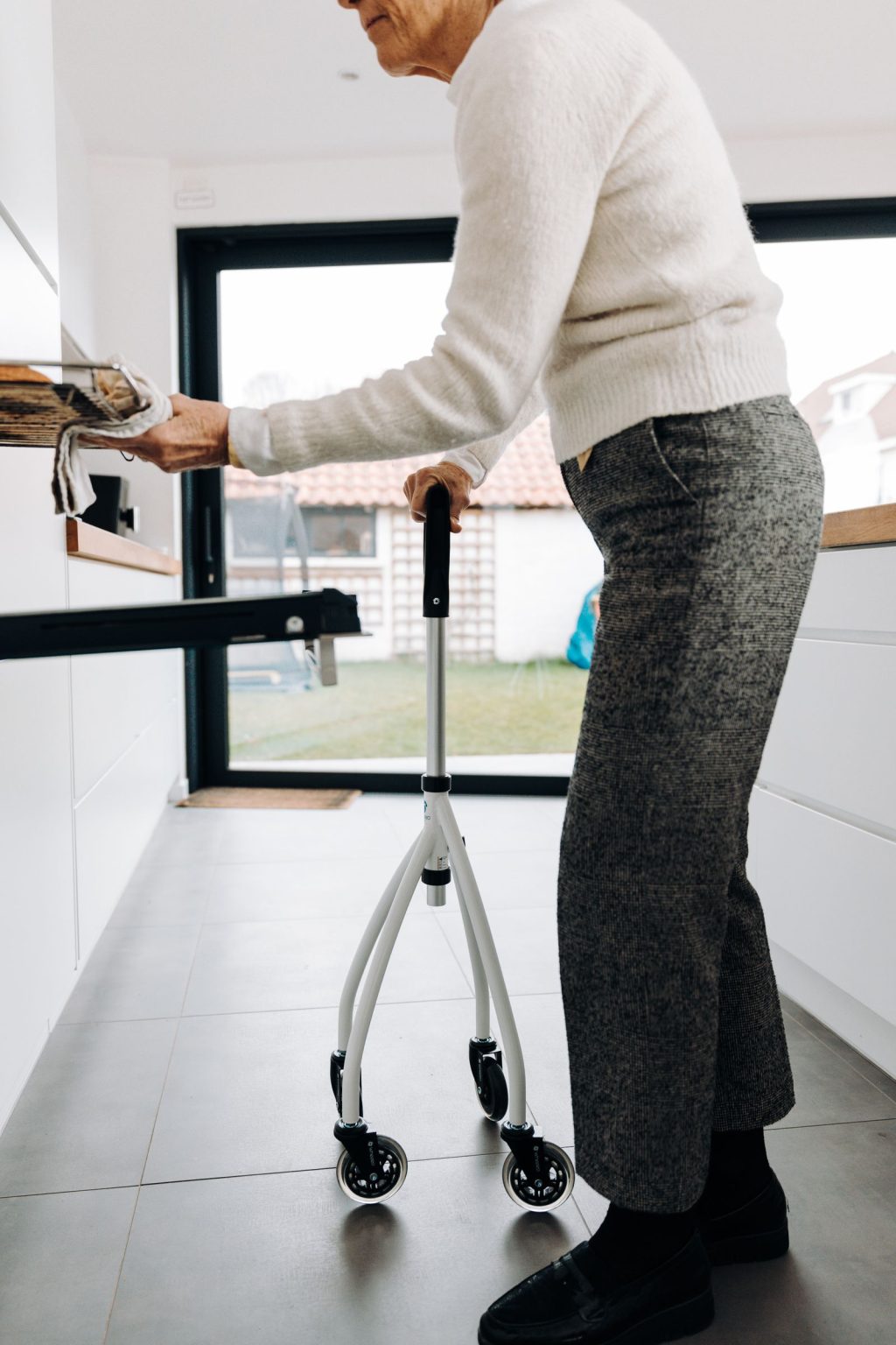 An older woman using a walker in a bright, uncluttered kitchen